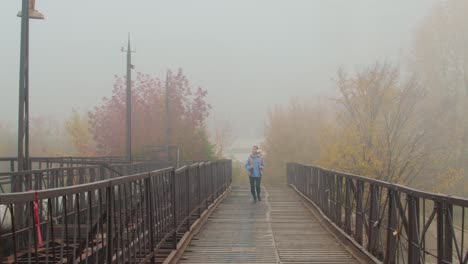 Chica-Rubia-Con-Auriculares-Corriendo-En-Un-Puente-De-Madera-En-Un-Día-Nublado