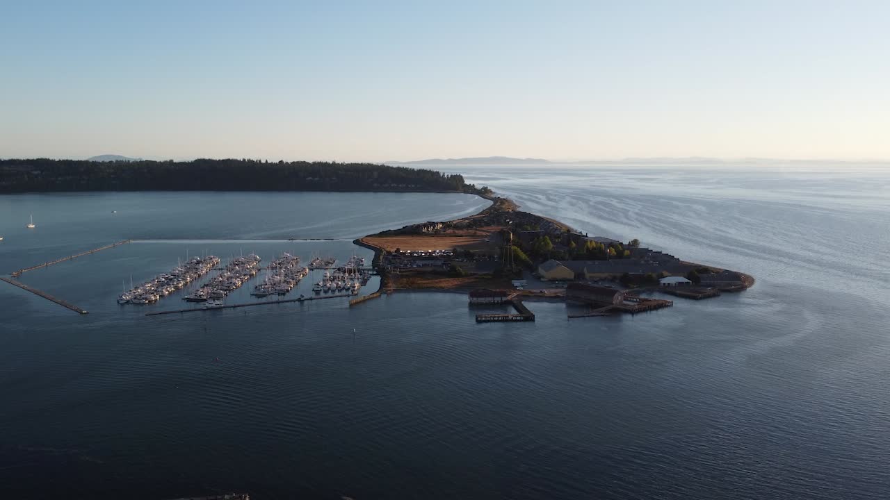 Semiahmoo’da gün batımında, turkuaz denizde seyreden teknelere bakan ve Semiahmoo tesisindeki eski bir su kulesinin önünden geçen limanın havadan görünümü, Washington, Seattle yakınları