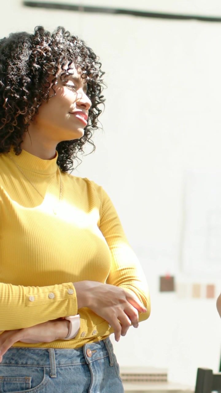 Vídeo vertical: Mulher sorrindo, inclinando-se para o orador após cumprimentá-lo na sala, com blusa amarela, relógio e espaço para texto.
