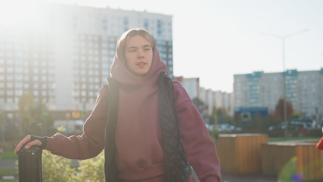 Resilient woman holds pull up bar and stretches side leg high under bright sun in urban park workout session, hoodie vest outfit highlighting strength flexibility focus during outdoor training