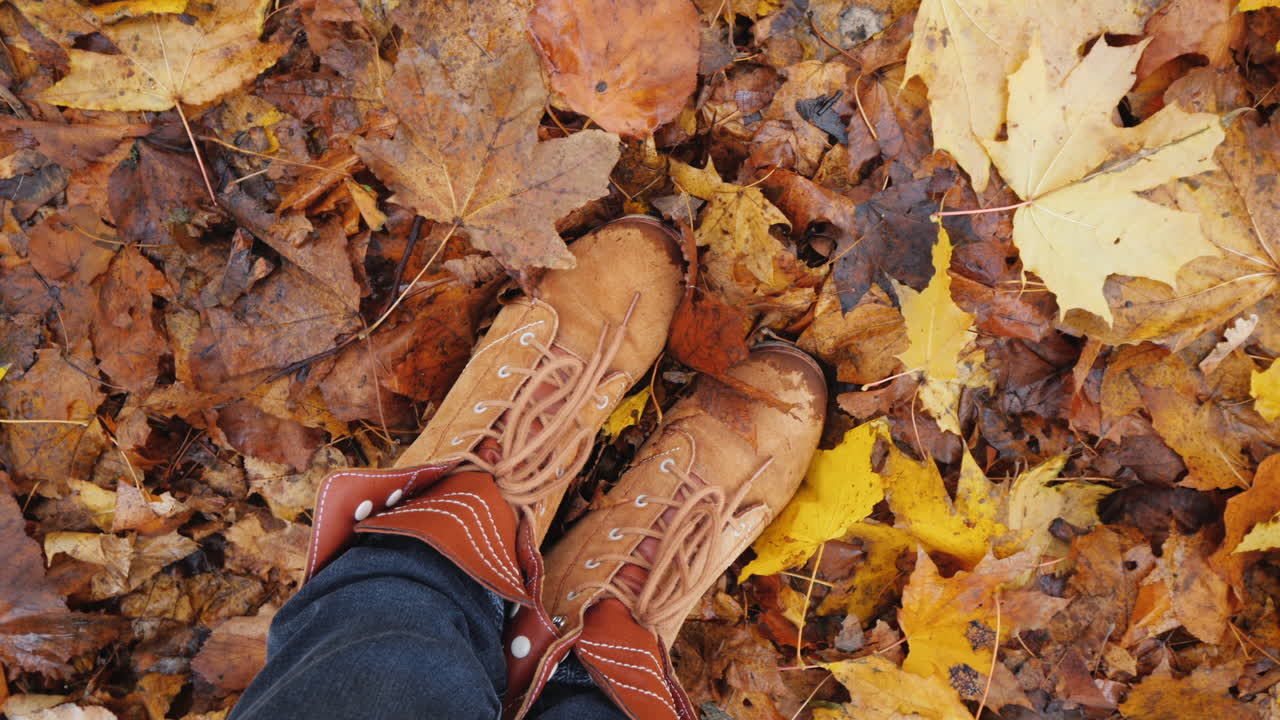 Piedi in stivali autunnali su foglie d'autunno cadute. La telecamera ruota.