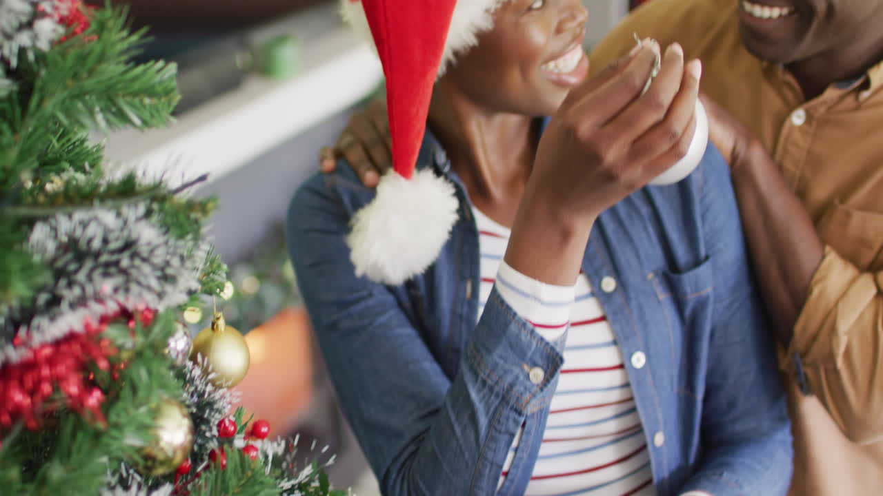 una feliz pareja afroamericana decorando el árbol de navidad.