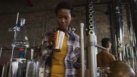 African-american-woman-working-at-gin-distillery-smelling-product-and-using-tablet