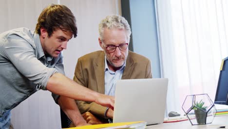 un hombre de negocios y un compañero de trabajo discutiendo en una computadora portátil.