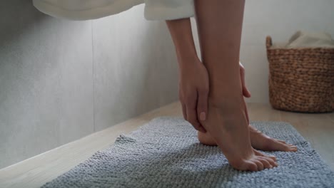 unrecognizable woman in bathrobe applying moisturizing cream on heels.