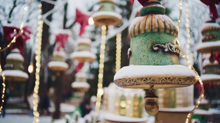 Primo piano di addobbi decorativi appesi, coperti di neve e circondati da calde lucine, in un contesto invernale all'aperto.