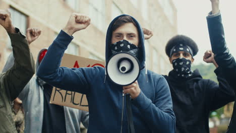 caucasian man yelling with arms up and talking on a loudspeaker in a protest with multiethnic group of people in the street