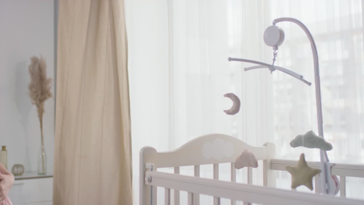 임산부가 아기 침대에 다가가 장난감을 돌리고 있다