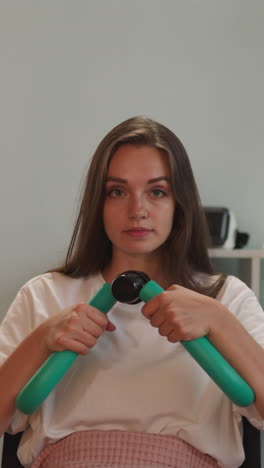 woman with disability with muscular dystrophy does exercise for arms. young female person sits in wheelchair training muscles in living room