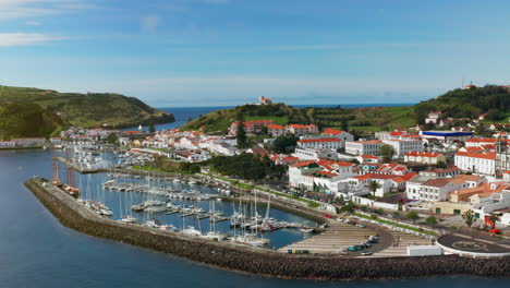 toma aérea cinematográfica de la pintoresca ciudad local de horta en la isla de faial, azores - portugal vista desde arriba de los barcos atracados en el puerto, paisaje verde en el fondo