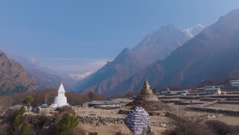drone shot of old buddhist stupa at phortse village, dry farming lands, layered blurry mountains, sunlight and untouched rocky himalayan nature dreamy clouds