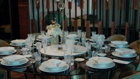 round table set with elegant white plates, crystal glassware, and floral centerpiece in a sophisticated indoor setting