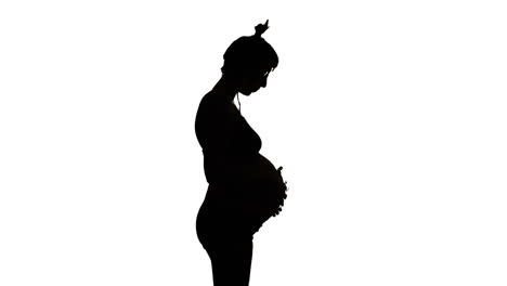 SILHOUETTE---A-heavily-pregnant-woman-looks-down-and-strokes-her-belly