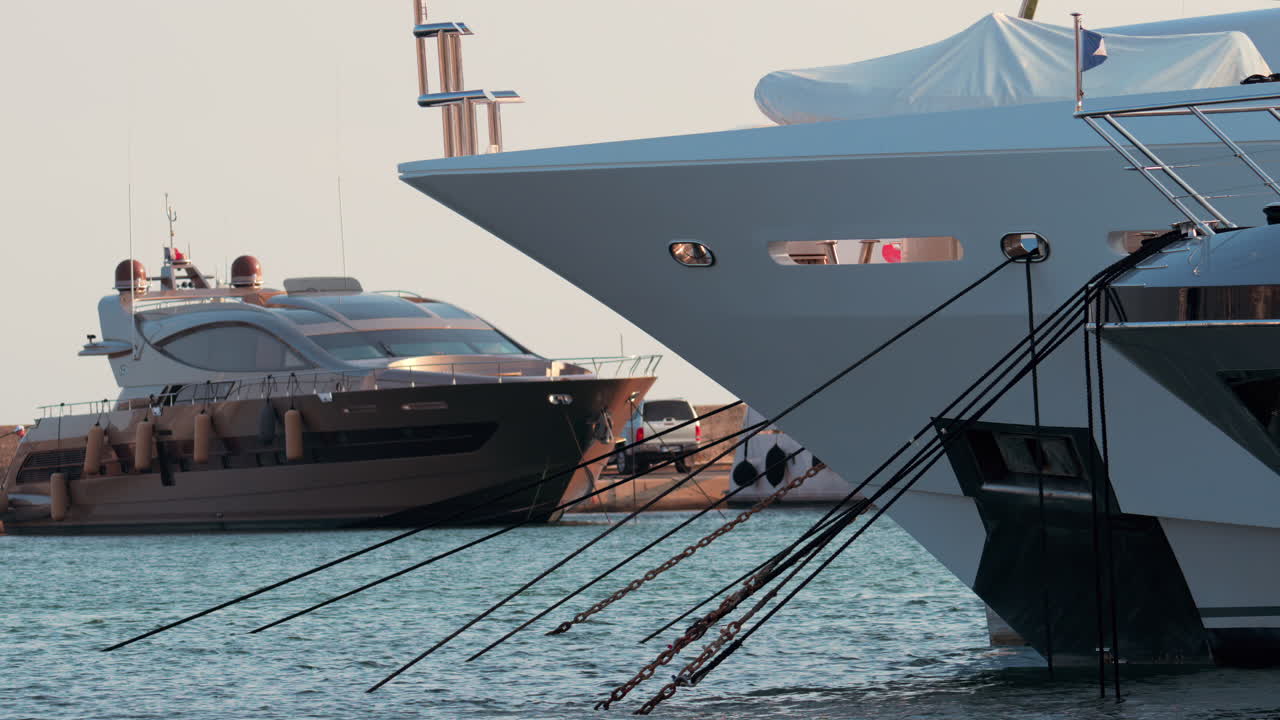 Close up of ropes and metal chains securing a luxury yacht in port, with blurred water and boats in the background
