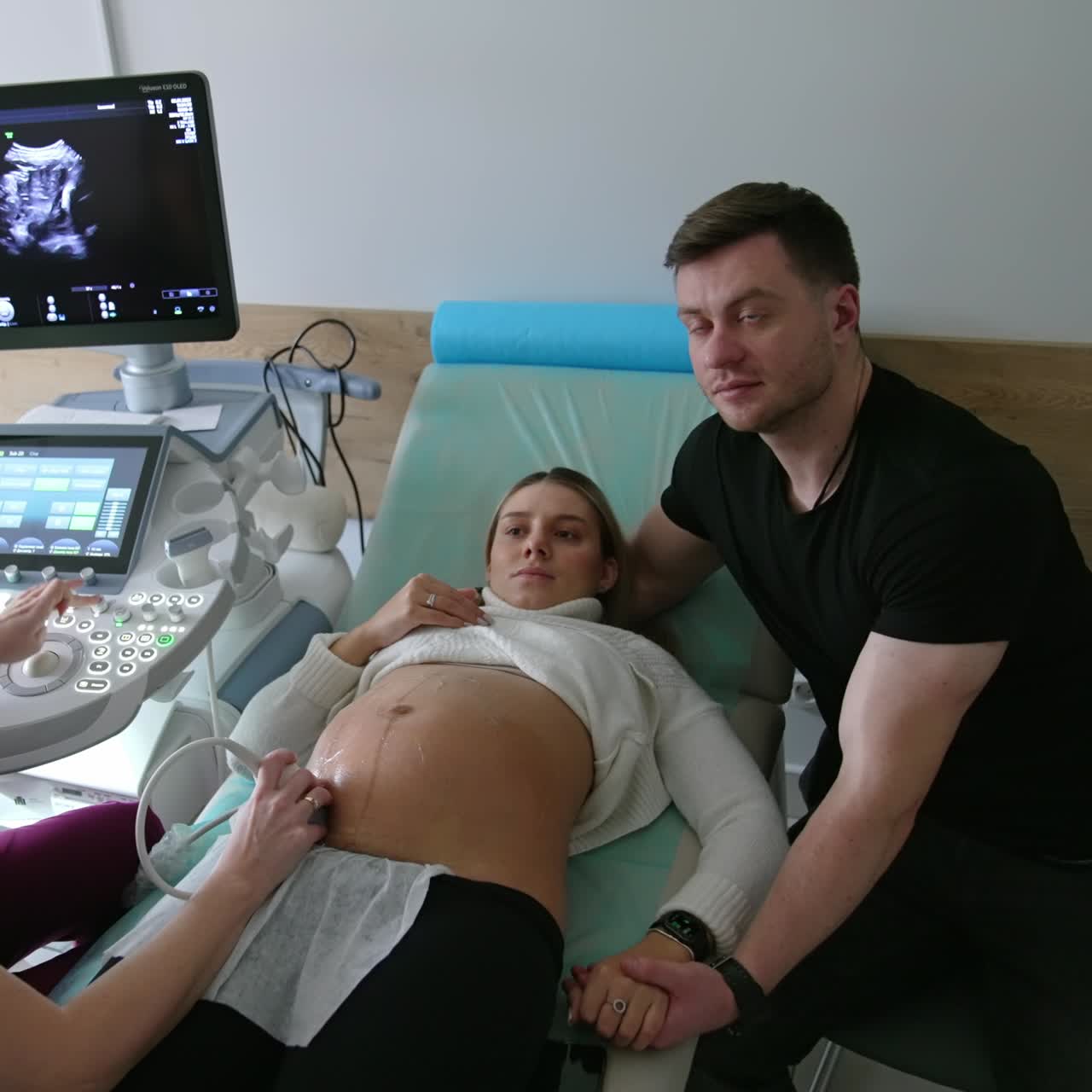 Doctor checks the pregnant woman on the ultrasound machine. Husband supports his wife holding by the hand. Top view