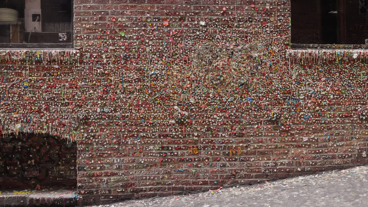 Fixed shot of a man walking past the famous gum-covered brick wall in Post Alley