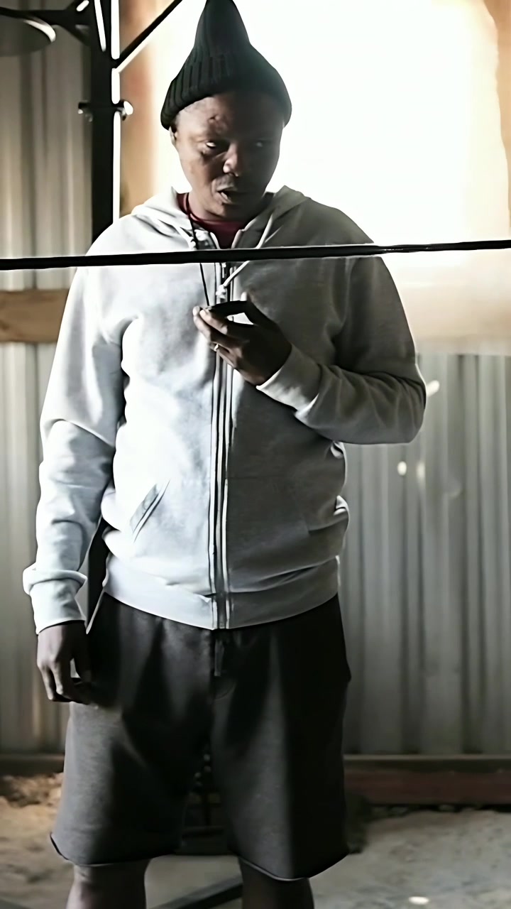 Vertical video: Reading hoodie-clad man holding device in shed, glancing at intruding arm past bar