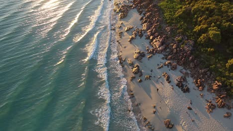 Aerial-View,-Lonely-Person-Walking-on-White-Beach-Sand-by-Ocean-Waves-on-Golden-Hour-Sunlight