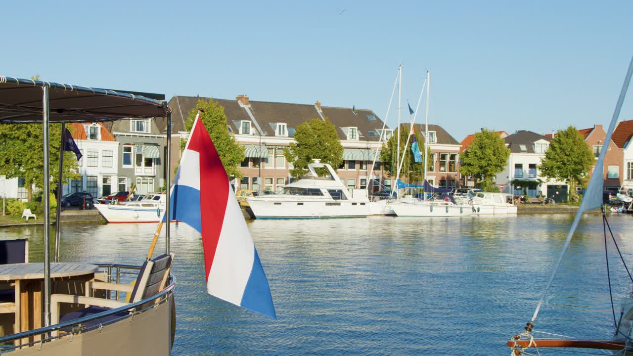 Dutch flag waving on boat along Haarlem canal, historic buildings and bridge in daylight