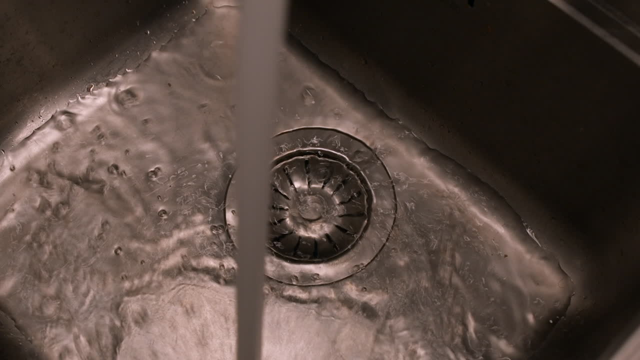 Close up detail: Stream of water flows from tap in steel kitchen sink