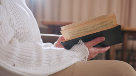 close up of visitor hands gently turning pages of book while seated indoors in soft natural light, wearing white knit sweater and beige pants, capturing calm atmosphere and slow reflective moment