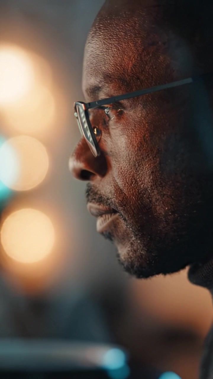 Close-up van een peinzend persoon in profiel met zachte achtergrondverlichting, die een moment van reflectie en introspectie vastlegt in een schemerig verlichte omgeving.
