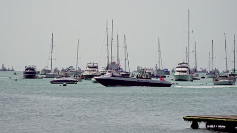 static shot of sail boats docked along the shore and a motor boat passing by in la punta, callao, peru on a bright sunny day