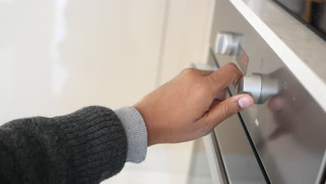 una mano girando el botón de un horno