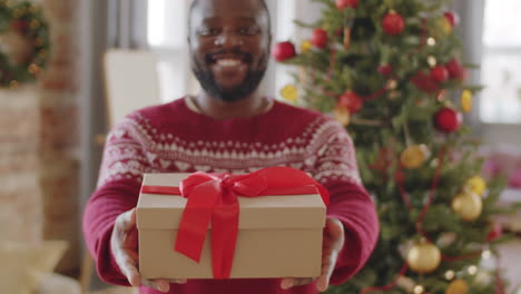 portrait of happy african american man with christmas gift at home