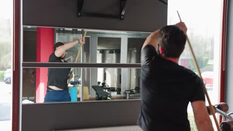 man do stretching warm up exercise with wooden stick in front of mirror