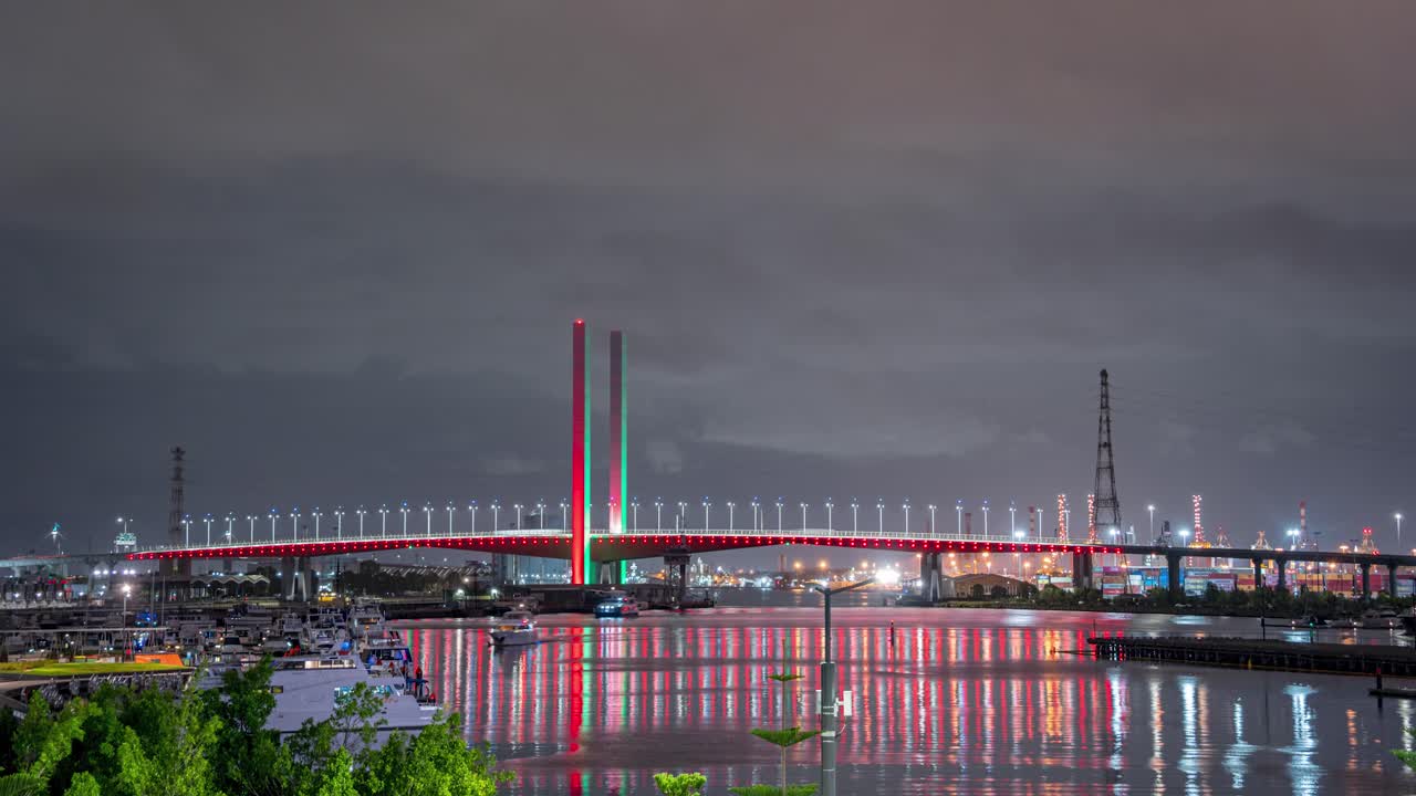 Night time lapse of Melbourne iconic Bolte bridge with shimmering red and green Christmas light projections and party boats cruising pass, located in Docklands waterfront harbour, Victoria, Australia.