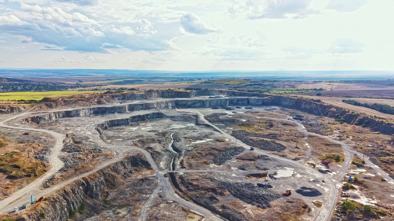 Granite quarry shows large open pit with machinery and trucks in action during daytime