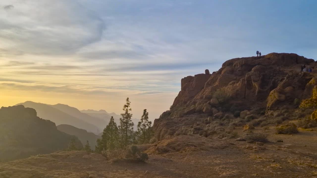 Splendido sole color oro che splende attraverso e dietro le montagne di Gran Canaria o delle Isole Canarie durante la sera o il tramonto, con le montagne che appaiono come silhouette e i raggi del sole visibili. Pini visibili.