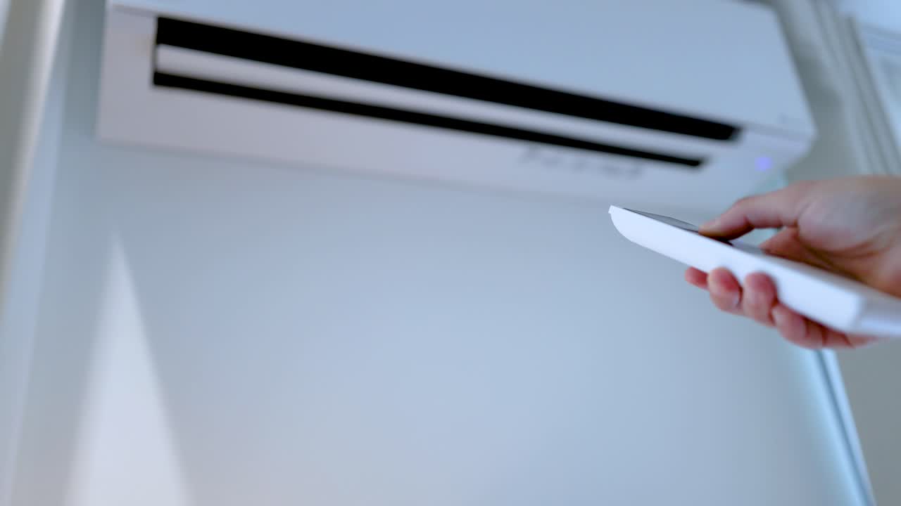 Een hand gebruikt een witte afstandsbediening om een wandgemonteerde binnenkoelunit in te stellen.