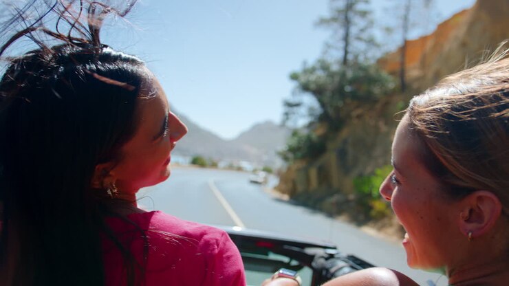 Amiche in piedi attraverso il tettuccio apribile di un'auto in viaggio attraverso la campagna