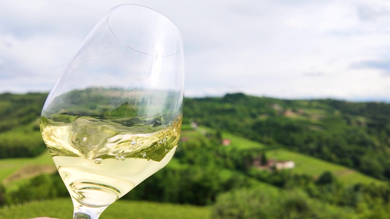 Primo piano di vino bianco che volteggia in un bicchiere sullo sfondo di dolci colline verdi di vigneti italiani.
