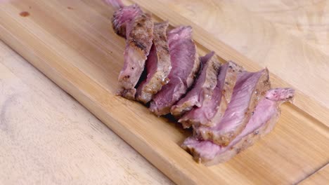 slow motion slider shot of placing sliced medium rare steak on a wooden serving platter