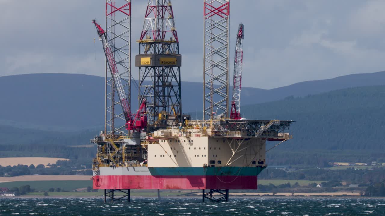 Stationær offshore-olieplatform i dagslys, bredt billede, urolig hav, skotsk højland i baggrunden