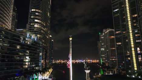 american flag waving in front of urban skyline in miami downtown at night