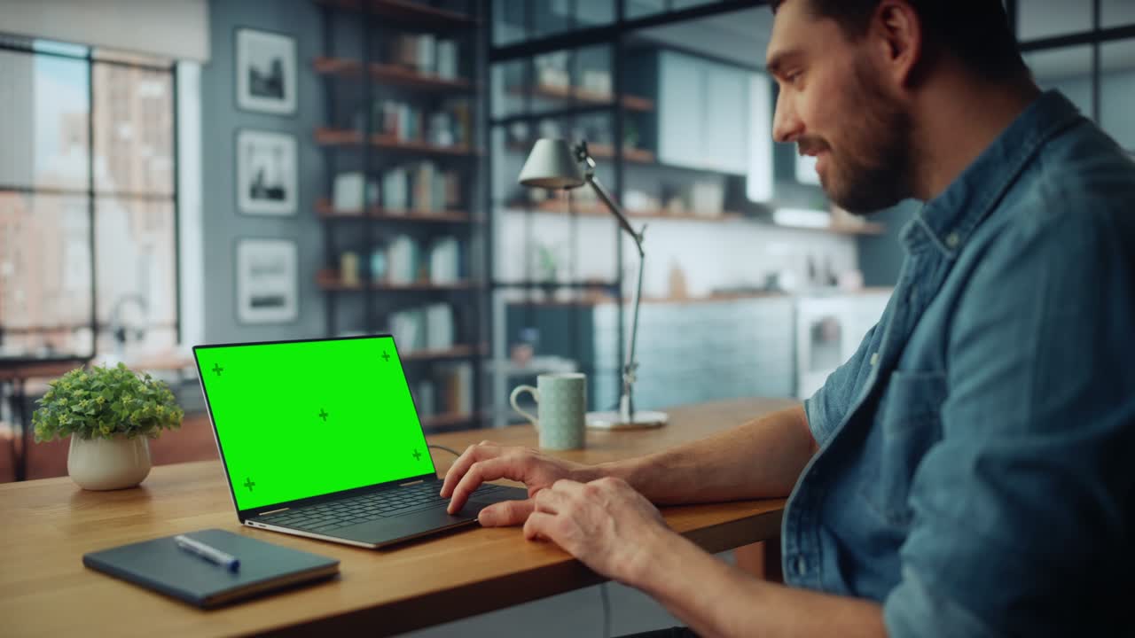 Handsome Caucasian Specialist Working on Laptop Computer with Green Screen Mock Up Display at Home Living Room. Freelance Man Chatting to Clients Over the Internet on Social Networks.