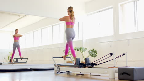 mujer caucásica con sostén rosa, leggings púrpura ejercicios en pilates reformador