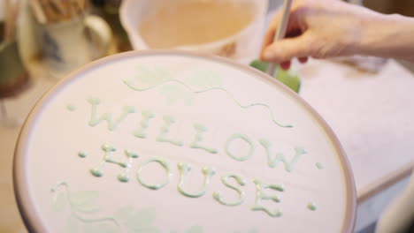 close up of male potter putting lettering onto clay plaque for house sign in ceramics studio