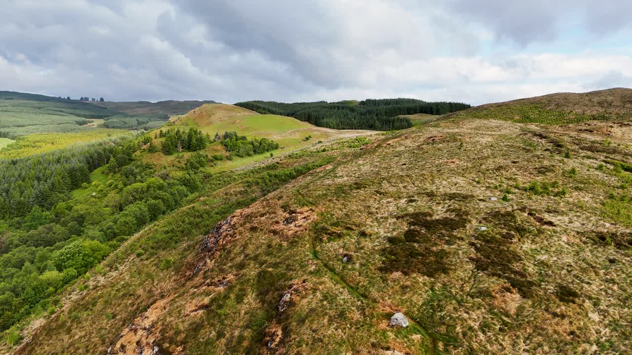 Drone following path, flying close to rocky hilltop, over ridge to reveal arboretum