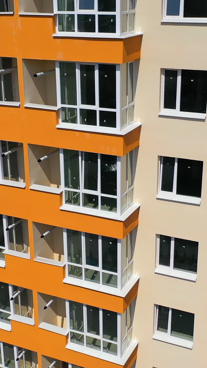 Building exterior of city multi-story apartment building. Facade of skyscraper building with new plastic windows and orange balconies at sunshine. Vertical video