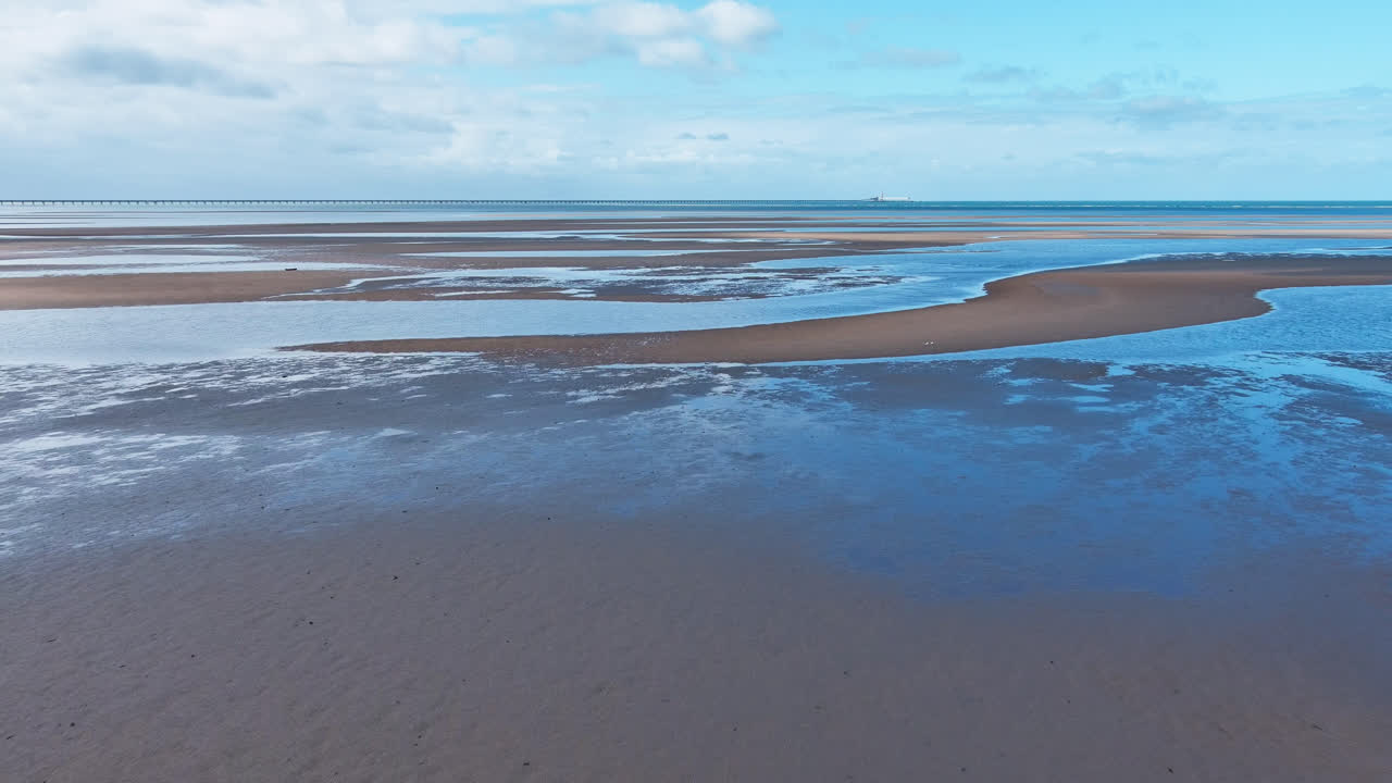 disparo aéreo, pista hacia adelante, ondas en el agua del océano de las piscinas de marea poco profundas de la playa del bosque con reflejo del cielo azul, extremo norte de queensland, australia