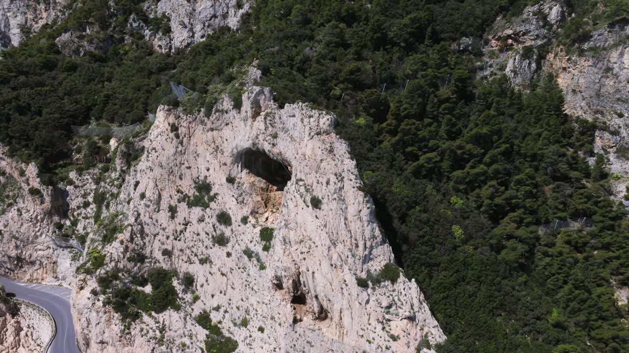 Aerial drone shot of rugged, vegetated Capo Noli promontory with ancient watchtower ruins overlooking the turquoise Ligurian Sea, Italy. [6, 9, 11, 22, 23, 25, 46, 50, 63]