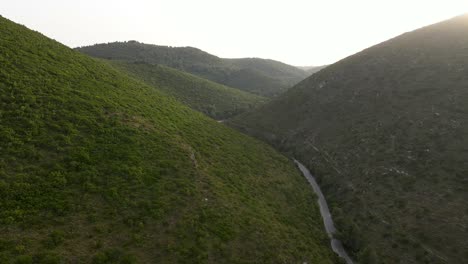 flight over a winding road in between the mountains in green valley at the greek island of zakynthos