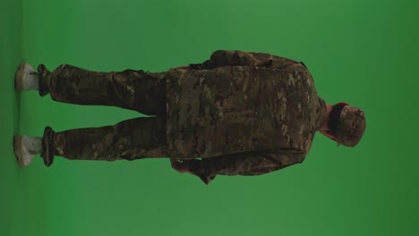full body back view of distressed asian male soldier looking around and shaking his head being sad due to the war while standing on the green screen background