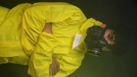 vertical hispanic scientist chemist crossing arms looking straight in to camera wearing respiratory gas mask, main character in dark smoke background in hazmat suit