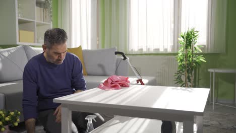 Middle-aged-man-using-cloth-to-clean-furniture-and-floor-in-living-room.